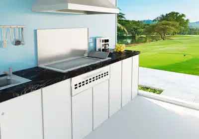 Stainless steel drop-in cooker set into a black granite countertop in a white outdoor kitchen overlooking a golf course