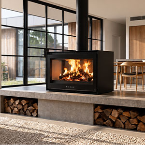 Forge F D80 double-sided freestanding fireplace on concrete plinth with log storage in bright open kitchen